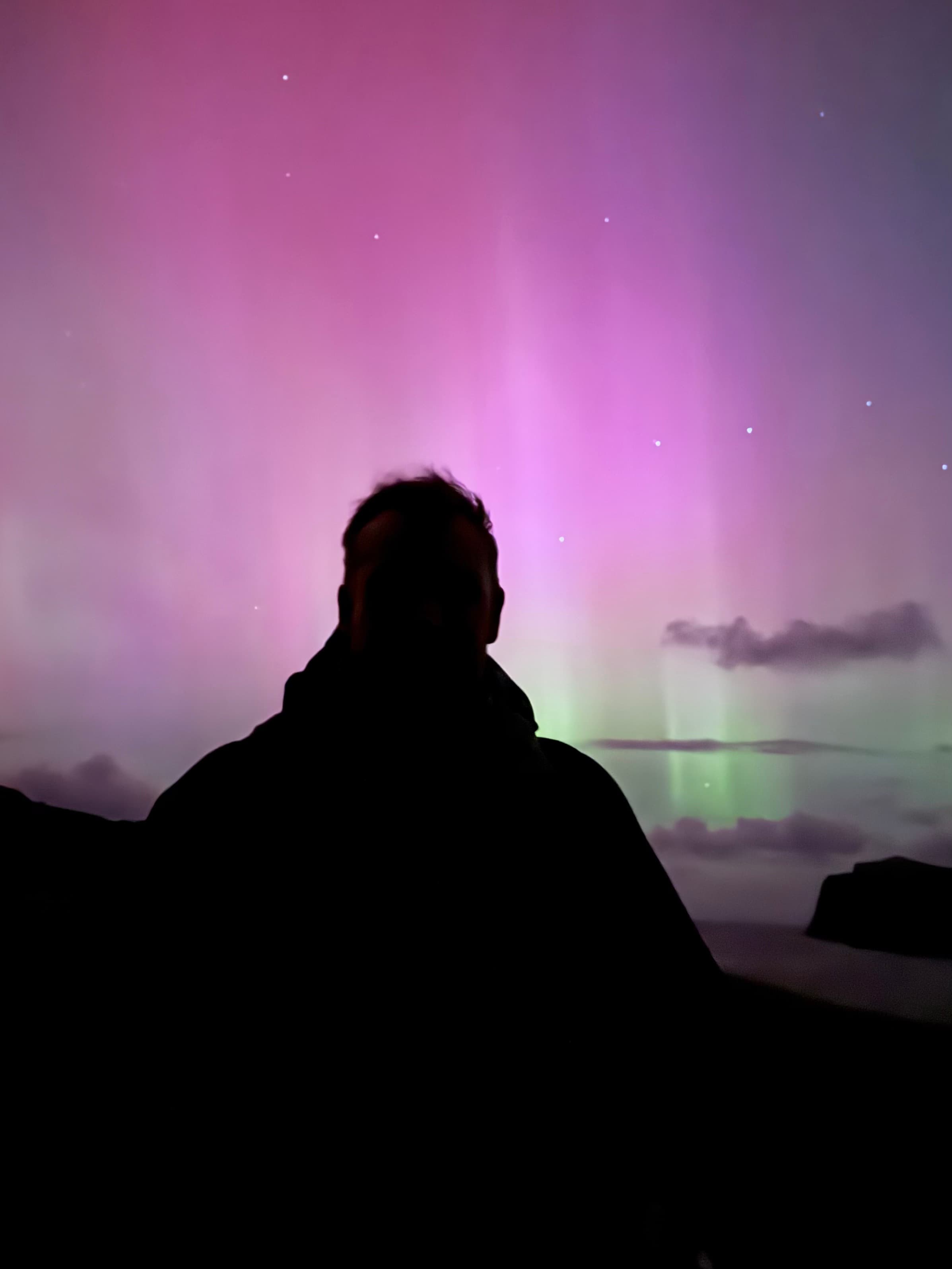 Breathtaking aurora borealis dancing across the dark sky above the rugged landscape of the Isle of Skye, with green and purple lights illuminating the Highland scenery